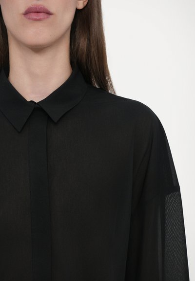 Zwarte doorschijnende blouse met een klassieke kraag, knopen aan de voorkant en gaaspanelen op de mouwen. Lichtgewicht stof met een zachte textuur.