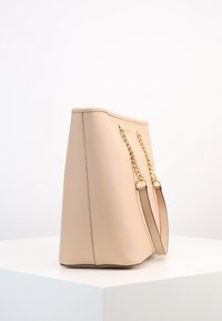 Borsa a tote in finta pelle beige con manici in catena dorata e silhouette strutturata. Presenta una texture liscia e un design minimalista.