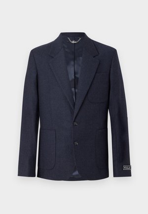 Blazer din lână bleumarin cu rever în formă de V, două buzunare frontale, închidere cu un singur nasture și căptușeală din satin. Are un eticheta de marcă pe manșetă.