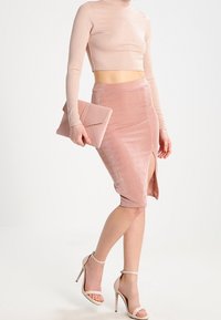Lichtroze ribgebreide lange mouwen crop top, fluwelen kokerrok met een zijsplit, hoge hakken en een bijpassende clutch.
