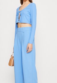 Jasnoniebieski, żebrowany krótki top z zawiązaniem z przodu, połączony z dopasowanymi spodniami z szerokimi nogawkami, które mają dwa guziki z przodu i boczne kieszenie.