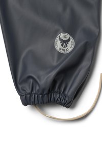 Gros plan d'une manche imperméable bleu foncé avec un poignet élastique et un logo circulaire de la marque Wheat représentant une tête d'élan et du texte.