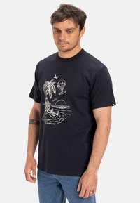 Navy cotton t-shirt featuring white graphic design of a palm tree, a parachute, and waves, with a round neckline and short sleeves.