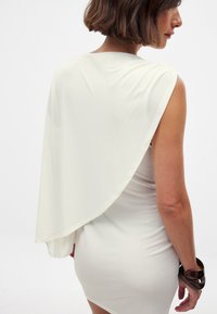 Valge kleit, mille taga on voolav rippuv kate, valmistatud siledast ja kerge materjalist. Disain on keha ümber vormiv ja ulatub keskmiselt reieni.