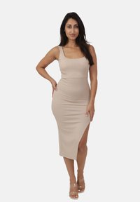 Abito midi rigato beige con scollo quadrato, silhouette aderente e uno spacco laterale. Il modello indossa tacchi trasparenti.