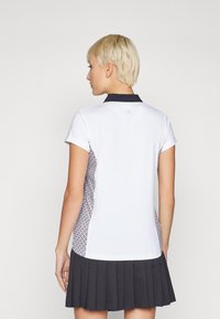 White polo shirt with a navy collar, featuring a patterned side panel. The shirt has short sleeves and is paired with a dark pleated skirt.