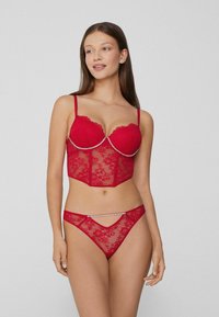 Czerwony zestaw bielizny z koronki, obejmujący bezramkowy gorset w stylu gorsetu z kwiatowymi wzorami i fiszbinami, w połączeniu z dopasowanym koronkowym stringiem. Uzupełniony kryształkami.