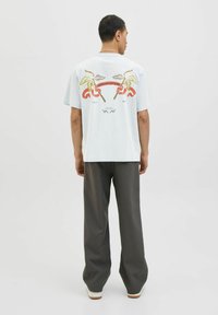 Lichtblauw t-shirt met korte mouwen en een grafisch ontwerp van palmbladeren, een lint en tekst op de achterkant, gecombineerd met een grijze broek.