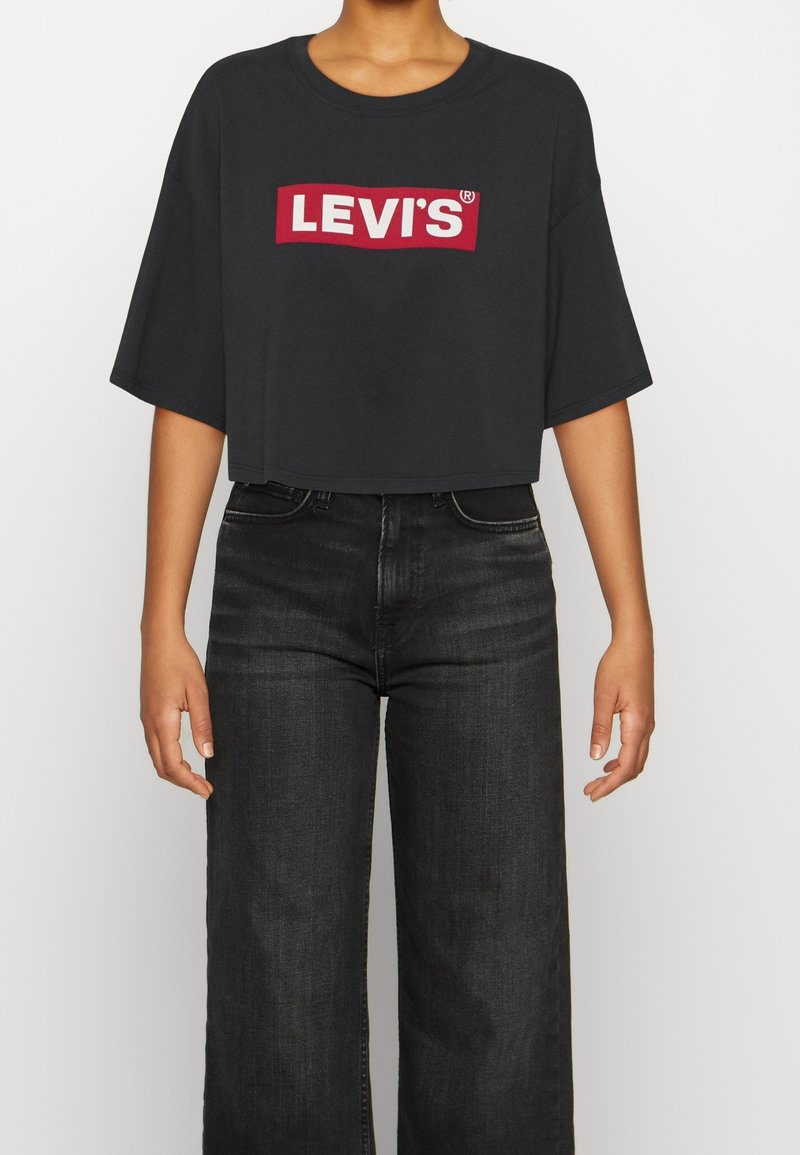 T-shirt crop noir en coton, avec un logo Levi's rouge et blanc sur le devant. Associé avec un jean en denim foncé taille haute.
