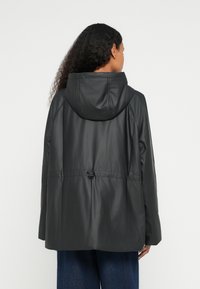 Μαύρο αδιάβροχο μπουφάν με κουκούλα, με σφιχτή μέση, λεία υφή και χαλαρή εφαρμογή. Χωρίς ορατά μεταλλικά μέρη ή σχέδια.