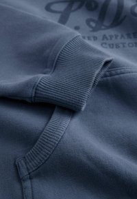 Navy blue sweatshirt featuring ribbed cuffs and pocket, made of soft, textured material with printed logo detail on the front.