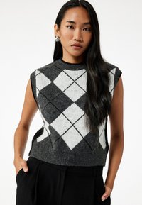 Suéter sin mangas en gris y blanco con patrón de diamantes, cuello redondo y dobladillo acanalado. Textura de punto, combinado con pantalones negros de cintura alta.