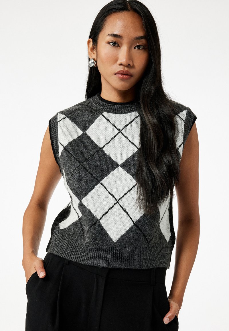 Suéter sin mangas en gris y blanco con patrón de diamantes, cuello redondo y dobladillo acanalado. Textura de punto, combinado con pantalones negros de cintura alta.
