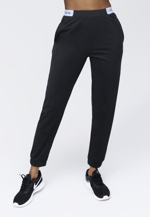 Schwarze Sporthose mit elastischem Bund und Bündchen, glattem Stoff, mit Seitentaschen und einem Logodetail am Bund.