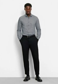 Button-up shirt in dark gray with a geometric pattern, paired with slim-fit black trousers and black shoes. Smooth fabric and regular collar.