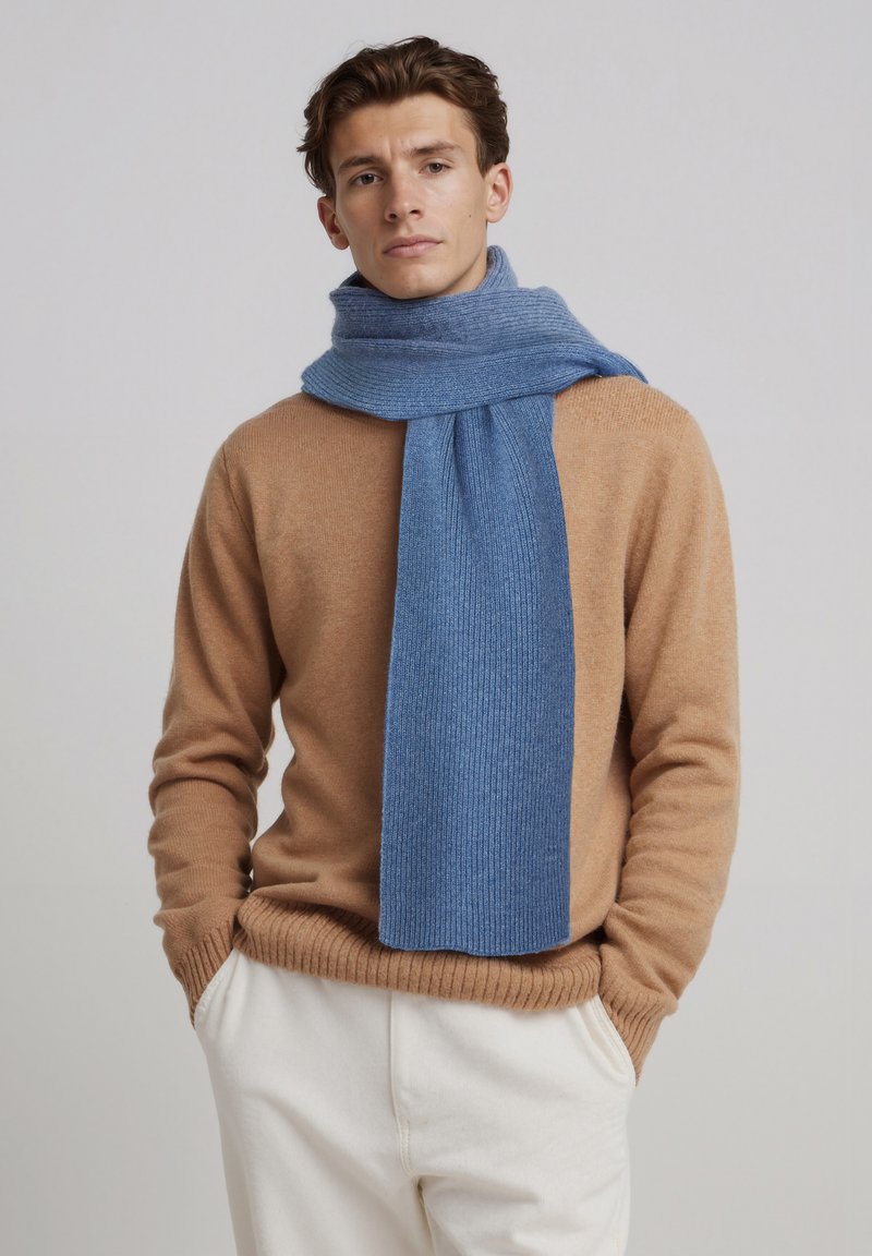 Écharpe côtelée bleu clair en tissu doux, drapée autour du cou. Portée avec un pull beige et un pantalon couleur crème.