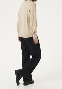Pull beige en maille douce, coupe ample, manches longues. Associé à un jean noir à jambes larges et à des bottes noires épaisses. Design minimaliste.