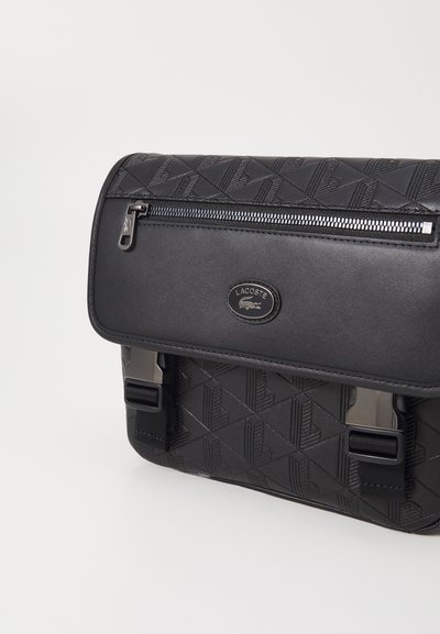 Sac messager noir avec une texture à motifs, doté d'un dessus zippé, d'une plaque logo et de clips ajustables sur les côtés pour une fermeture sécurisée.