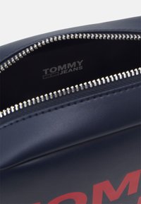 Borsa sintetica blu navy con zip argentata, dotata di un logo stampato all'interno. Texture liscia e forma rettangolare con apertura superiore.