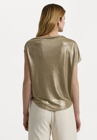 Metallisch goldenes Kurzarm-Oberteil mit lockerem Schnitt, gerundetem Rücken und glatter Textur. Der glänzende Stoff fängt das Licht ein.