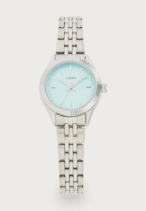 Stříbrně tónovaný hodinky Timex se světle modrým ciferníkem a stříbrným náramkem. Obsahuje texturovaný rámeček, indexy hodin a tři ručičky pro zobrazení času.