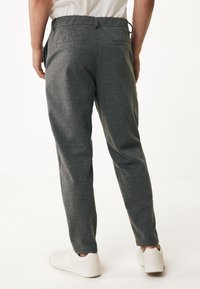 Grijze, rechte broek van een textiele stof met elastische tailleband. Voorzien van twee achterzakken en gedragen met witte sneakers.