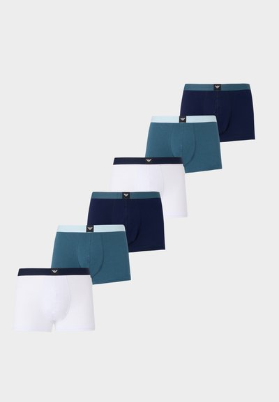 Έξι ζευγάρια ανδρικά μπόξερ σε εναλλασσόμενα λευκό, τυρκουάζ και ναυτικό μπλε, διατεταγμένα διαγώνια πάνω σε ανοιχτό γκρι φόντο.