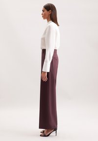 Witte textuur blouse met lange mouwen, gecombineerd met hooggeprofileerde, rechte maroon broek. Model draagt zwarte open teenhakken.