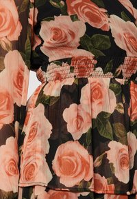 Blommig klänning med svart bakgrund och stora persika-rosor samt gröna blad. Lättviktig tyg med samlad midja och plisserad kjol.