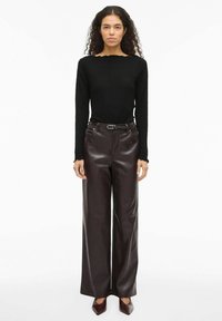 Czarna prążkowana bluzka z długim rękawem i karbowanym dekoltem, zestawiona z brązowymi skórzanymi spodniami o szerokich nogawkach i brązowymi butami na czubku.