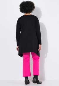 Tunique noire à manches longues avec un ourlet incurvé associée à un pantalon ajusté rose vif et des bottines noires à clous. Tissu texturé, design moderne.