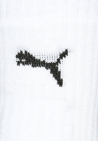 Weißer Strickstoff mit einem schwarzen grafischen Design, das einer abstrakten Form oder einem Logo ähnelt. Die Textur erscheint weich und hat eine dehnbare Qualität.