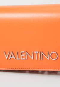 Valentino peněženka ve světlé oranžové kůži se hladkým povrchem, s kovovými prvky ve stříbrné barvě s logem značky na přední straně.