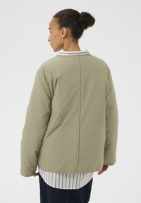 Hellgrüne Steppjacke mit rundem Kragen, überschnittenen Schultern und glatter Textur, getragen über einem weiß-blau gestreiften Hemd.