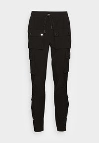 Svarta cargobyxor med flera fickor med lock, elastisk midja med dragsnöre, och tryckknappar längs anklarna.