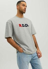 Šedé tričko s krátkym rukávom a okrúhlym výstrihom s písmenami "R.D.D." v červenej a námorníckej modrej farbe cez prednú stranu. Voľný strih, bavlnený materiál.