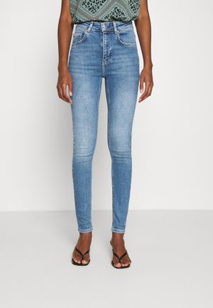 Jeans ajustados de tiro alto en azul claro, con una textura de mezclilla suave y diseño de cinco bolsillos, combinados con una blusa estampada y chanclas.