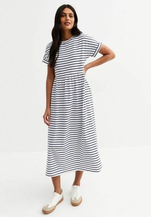 Striped cotton maxi dress in white with navy horizontal stripes, short sleeves, elastic waist, and flowing silhouette, paired with white sneakers.