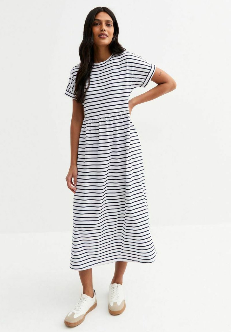 Abito maxi in cotone a righe bianche con righe orizzontali blu navy, maniche corte, vita elastica e silhouette fluida, abbinato a sneaker bianche.