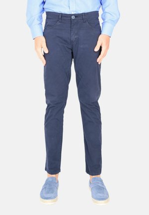 Chino da uomo blu navy in cotone, con vestibilità slim, chiusura a bottoni e tasche frontali. Indossati con scarpe slip-on azzurre.
