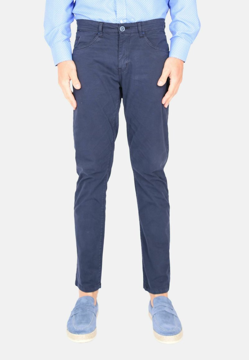 Chino da uomo blu navy in cotone, con vestibilità slim, chiusura a bottoni e tasche frontali. Indossati con scarpe slip-on azzurre.