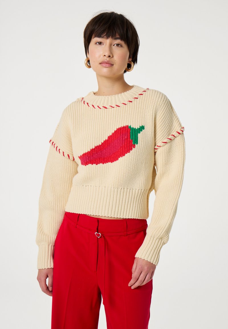 Crèmekleurige gebreide trui met een afbeelding van een rode chilipeper, verfraaid met een rode rand langs de halslijn en mouwen.