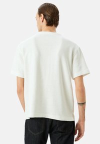 Hvid t-shirt med korte ærmer og rund hals, lavet af blødt stof, med en afslappet pasform og minimalistisk design. Ingen synlige mønstre eller detaljer.