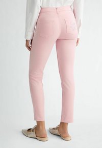 Ružové priliehavé džínsy s vreckami na zadnej strane, vyšívanými detailmi a hladkým povrchom. V páre s plochými slip-on topánkami.