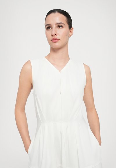 White sleeveless dress with a V-neckline, pleated waist, and side pockets. Made of lightweight fabric, featuring a subtle sheen and simple design.