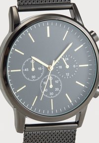 Montre en acier inoxydable noir avec un cadran gris, trois sous-cadrans et aiguilles dorées. Elle est dotée d'un bracelet en maille et de marqueurs lumineux.