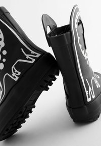 Bottes de pluie en caoutchouc noir avec des motifs animaux blancs, semelles texturées et languettes de tirage. Forme chunky avec une finition brillante et une semelle extérieure rainurée.