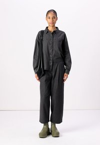 Camisa de manga longa em denim escuro, calças largas correspondentes e calçado de borracha verde. Design simples com botões e um ajuste descontraído.
