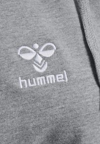 Grijze stof met wit geborduurd merklogo met een gestileerde bij en het woord "hummel" eronder.