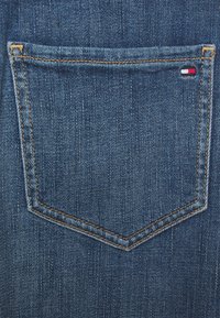 Denim tyg bakfickan av blå jeans, med orange sömmar och en liten röd, vit och blå logotagsmärke. Texturen är slät med vertikala linjer.